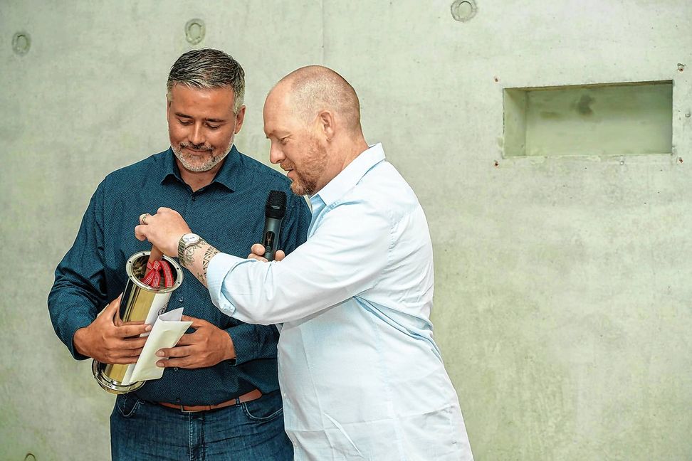 Die Schulleiter Jörg Gerspach (links) und Felix Bubner befüllen die Zeitkapsel, die in eine Wandnische eigebaut wird.