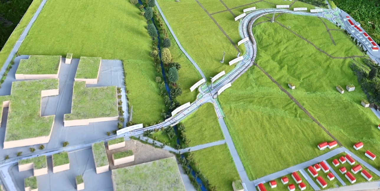 Die Osttangente im Modell. Sie überquert aus dem Gewerbegebiet Ost (links unten) kommend (Hutwiesenstraße) auf einem Damm den Planbach im Hölzertal, führt in einer Schleife um den Gollenberg herum und mündet an einem Kreisverkehr (rechts oben), von dem aus auch die Zufahrt zum Sportgelände an den Buchen abgeht, in die Alte Stuttgarter Straße. Auf dieser geht es weiter zum Aspenschopf in Richtung Stuttgart und Sindelfingen oder auf die Südtangente in Richtung B 464. Die Häuserzeile am rechten Bildrand gehört zum innerörtlichen Teil der  Alten Stuttgarter Straße. Bild: Reichert