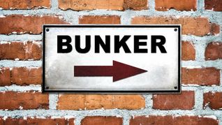 Ein Wegweiser zum Bunker an einer Ziegelwand.