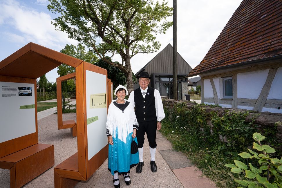 Das Waldensermuseum (rechts) in Neuhengstett mit Pavillon dahinter und Themengarten links. Davor Dieter und Hannelore Rapp in der Tracht der Waldenser. Für die Frauen galt: schwarzes Kleid mit Stehkragen und Schürze. Ein Fransenschal zu einem Dreieck gefaltet. Die Männer trugen Kniebundhose mit weißem Leinenhemd und ärmelloser Weste. Bild: Richter