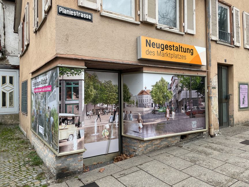 In den Schaufenstern sieht man, wie der Marktplatz einmal aussehen soll. Bild: z