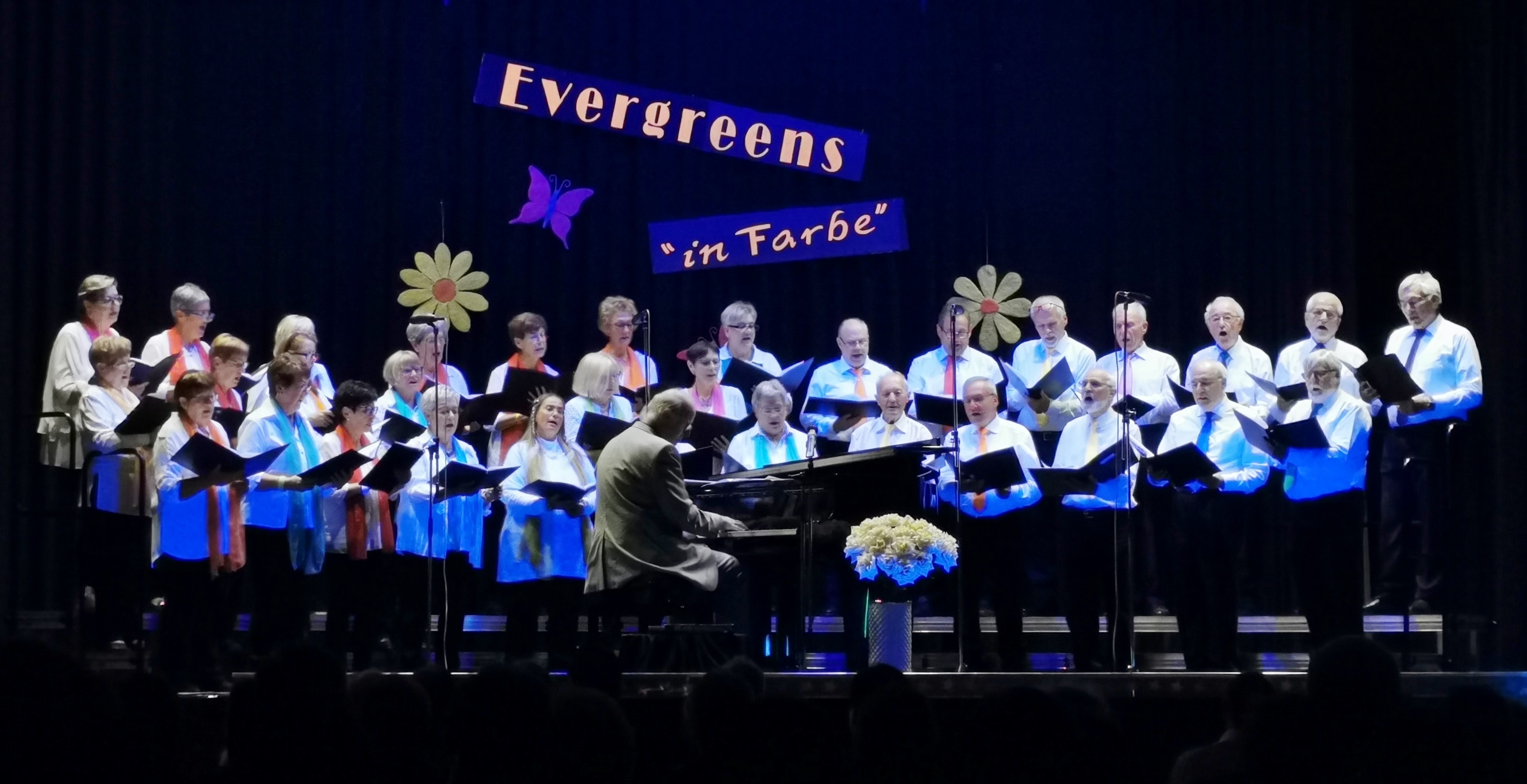 Die Sängerinnen und Sänger des Dahersheimer Liederkranzes auf der mit Schwarzlicht beleuchteten Bühne in der Festhalle. Bild: z