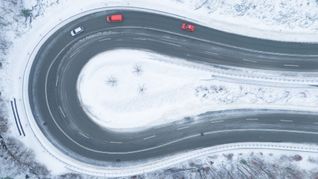 Autos fahren auf einer von Schnee geräumten Serpentine entlang. (Luftaufnahme mit einer Drohne).