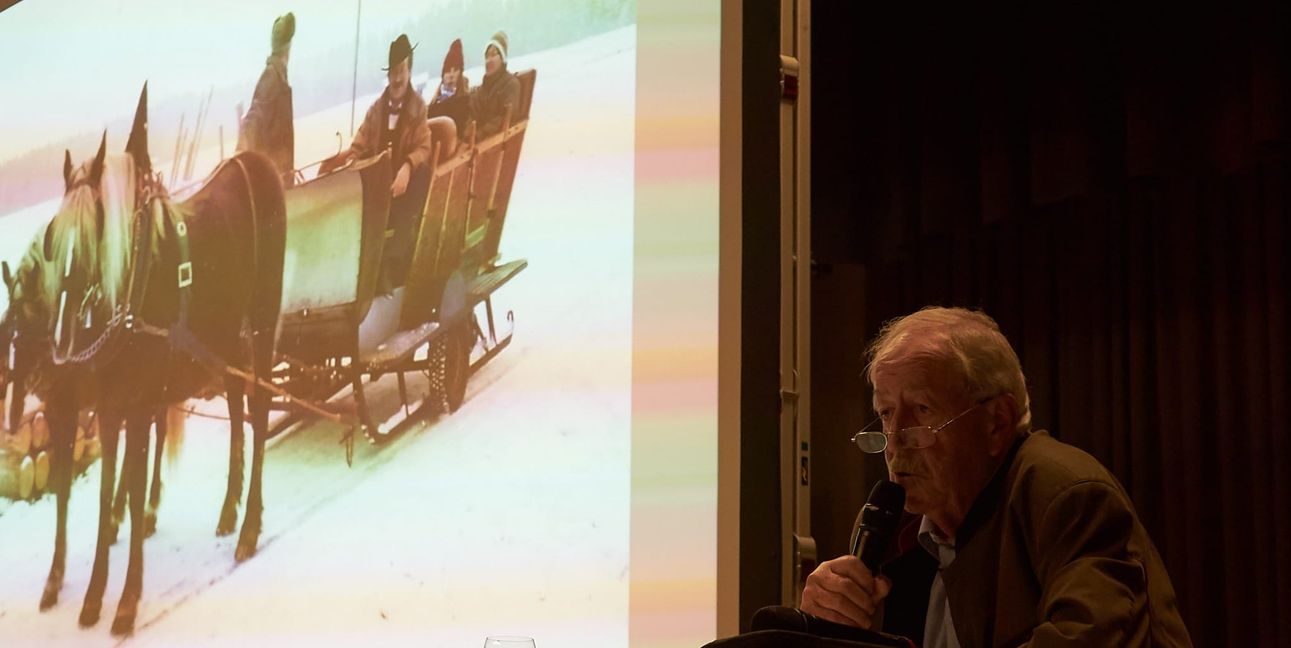 Walter Arnold bei seinem Vortrag am Tisch und auf dem Bild seitlich auf dem Pferdeschlitten.