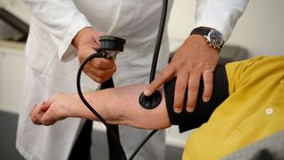 Ein Hausarzt misst in seiner Praxis einer Patientin den Blutdruck
