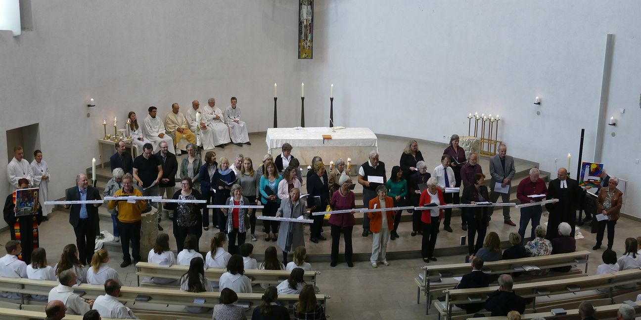 Die Martin-Luther-Gemeinde (links mit Pfarrerin Eva Schury) grüßt St. Klemens (Pfarrer Dietrich Groh mit dem Bild der katholischen Kirche), dazwischen die Gäste mit den Schokoladeriegeln