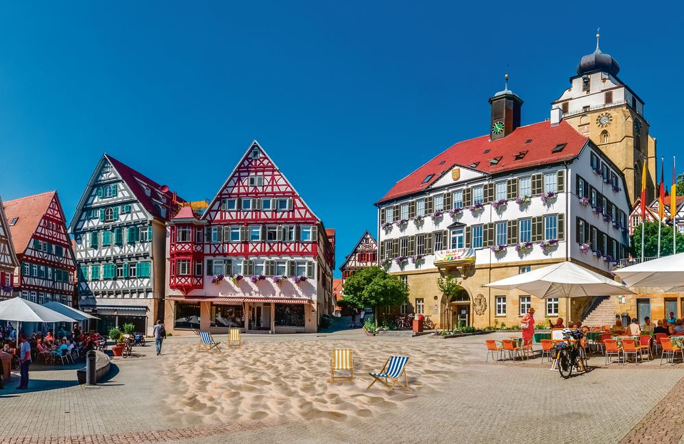 Sommer, Sand und mehr: Auf dem Herrenberger Marktplatz soll zur Haupturlaubszeit ein künstlicher Strand aufgeschüttet und „bespielt“ werden.    Montage: Sina Ettmer – stock.adobe.com/gb