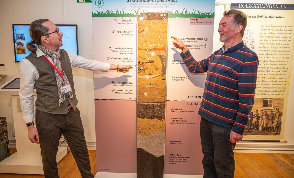 Christoph Lehnert (links) und Heinz Lüdemann vor der stratigraphischen Säule: Diese veranschaulicht die verschiedenen Bodenschichten, die sich im Lauf der Zeit übereinander abgelagert haben.