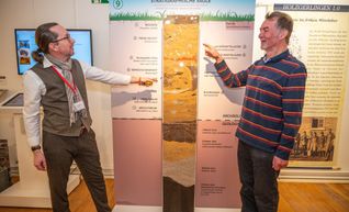 Christoph Lehnert (links) und Heinz Lüdemann vor der stratigraphischen Säule: Diese veranschaulicht die verschiedenen Bodenschichten, die sich im Lauf der Zeit übereinander abgelagert haben.