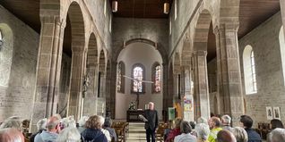 Immanuel Rühle, bei seiner ersten Führung nach sieben Jahren in der Martinskirche Sindelfingen. Der Chef des Stiftungsbeirats stellt die Themen für das Stifterfest vor, nämlich die Taube-Skulptur von Frank Teufel über ihm und die Bleiglasfenster von Walter Kohler in der Mittelapsis der Kirche.