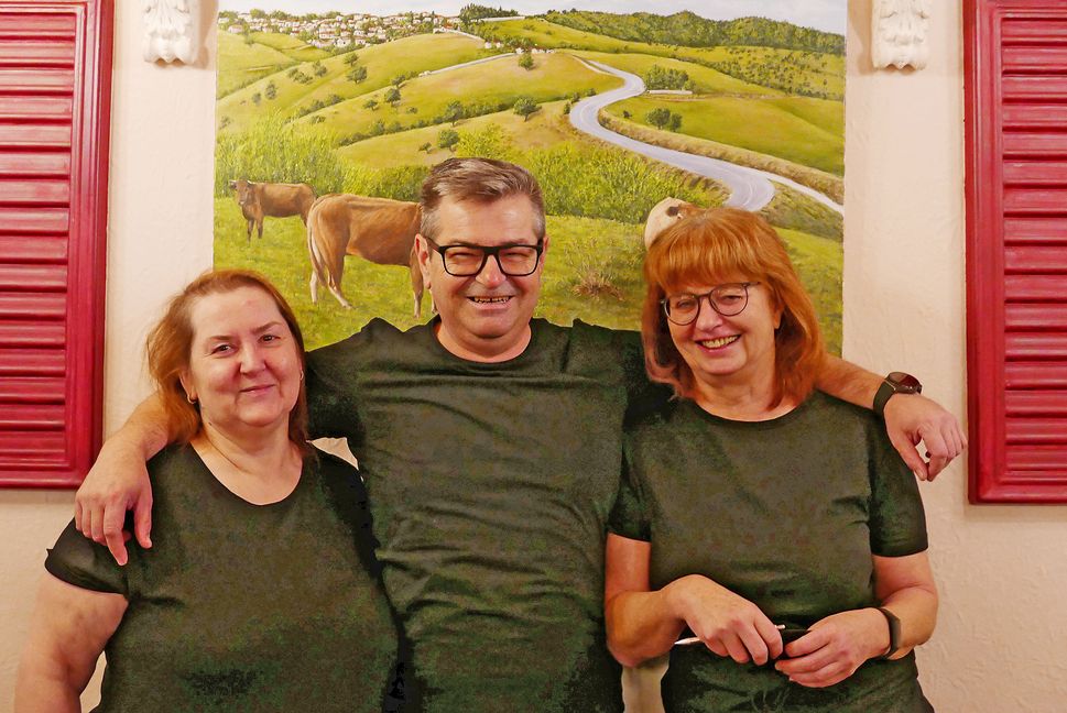 Maria Gatsiou, Efthimios Gatsios und Brigitte Gatsios-Daubner vor dem Gemälde mit dem Heimatdorf der griechischen Gastronomen, das im Maichinger Restaurant Hellas hängt. Bild: Jung