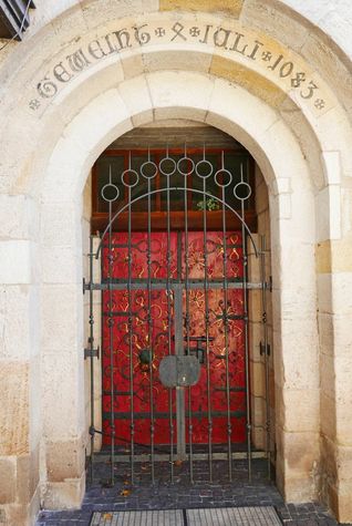 Die blutrote Tür mit ihren gusseisernen und bronzenen Beschlägen ist eines der schönsten Details der Sindelfinger Martinskirche, die 1083 geweiht wurde. Wahrscheinlich war das Gotteshaus damals noch eine Baustelle, denn Untersuchungen der Jahresringe haben ergeben, dass das Holz für den Dachstuhl erst im Jahr 1131 geschlagen wurde. Auffällig am Westportal mit seinen vielen Beschlägen ist der Löwenkopf mit dem eisernen Ring im Maul. Der Löwe steht symbolisch nicht nur für den Evangelisten Markus, sondern vor allem für Christus, dem Löwen von Juda. Der eiserne Ring im Löwenmaul selbst war einst die letzte Rettung für Verfolgte. Es ist der Gnadenring, der Asylring. Demjenigen, der ihn ergriff, garantierte er zumindest Kirchenasyl.
