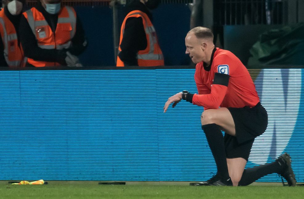 Schiedsrichterassistent Christian Gittelmann hat seine Fahne verloren und kniet auf dem Rasen, nachdem er einen Becher an den Kopf bekommen hatte.