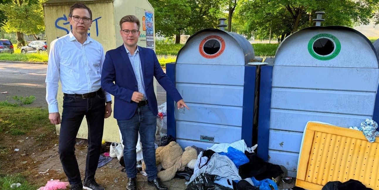 Dr. Markus Fritz und Max Reinhardt (rechts) vor einem Altkleidercontainer mit wildem Müll in der Pfarrwiesenallee.
