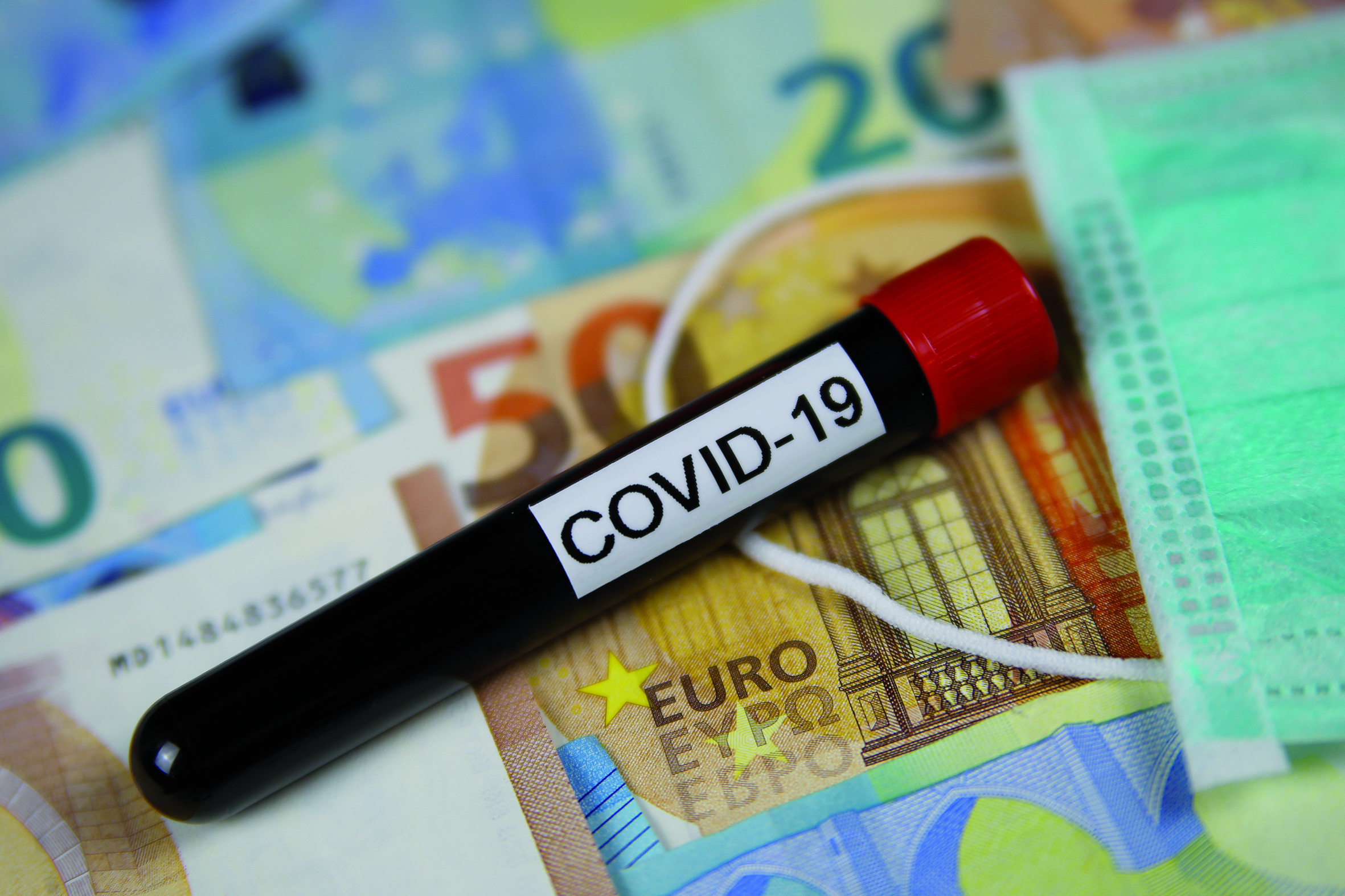 Corona virus uncertain consequential costs concept symbol: closeup of isolated blood sample vial on euro paper money bank notes und surgical mask