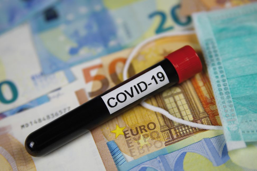 Corona virus uncertain consequential costs concept symbol: closeup of isolated blood sample vial on euro paper money bank notes und surgical mask