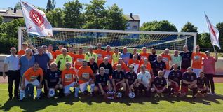 Die Teams vor dem Anpfiff mit OB Dr. Stefan Belz, Uschi Russell, Massimo Lampugnani, Domenico Boeri (von links ohne Trikot) und Carmelo Franchesini (links im gelben Schiedsrichterdress), sowie Ron Russell (ganz rechts). Das Team der Kanne-Knobler (orange Trikots): Vincent Fleck, Team-Manager Thomas Schulz, Alexander Popov, Vladimir Harachasch, Vitaly Kurkov, Ralf Allgöwer, Thomas Fritz, Martin Oßwald, Karsten Zink, Frank Sieber (hinten von links), Lothar Wanner, Axel Arndt, Fabian Rau, Torwart Peter Böttinger, Steffen Müller, Karl Ruthardt und Dieter Wünsch (vorne von links). Auf dem Bild fehlt Trainer Josef Stegemann.