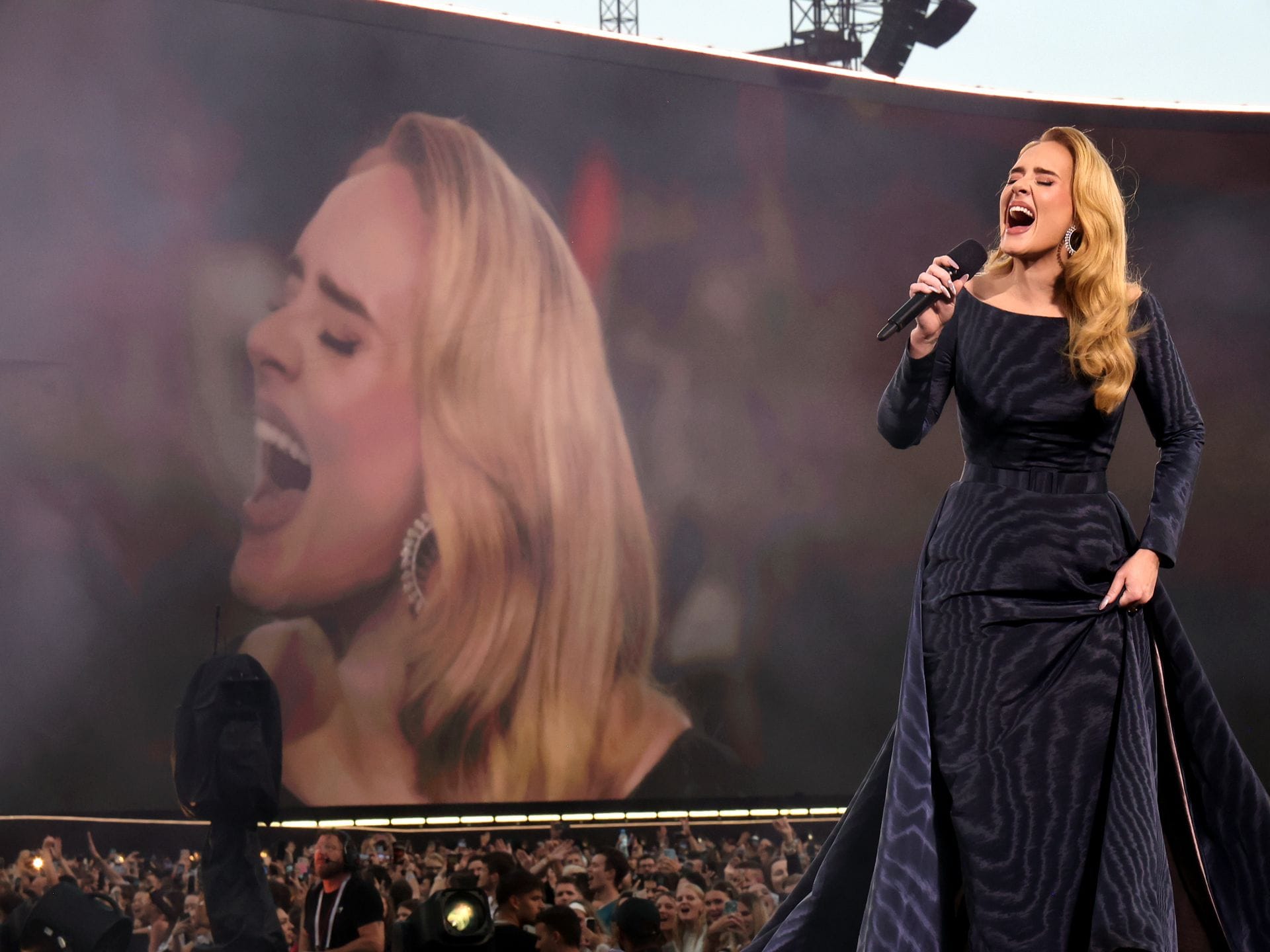 Im Vordergrund singt Adele. Im Hintergrund ist die Sängerin auf einem überdimensionalen Monitor zu sehen.