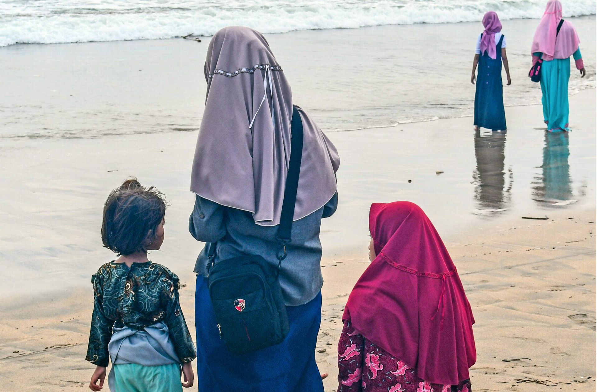 Frauen mit Kopftüchern am Strand in Kuta auf Bali. In Indonesien herrschen teilweise strikte Kleiderordnungen für Frauen.