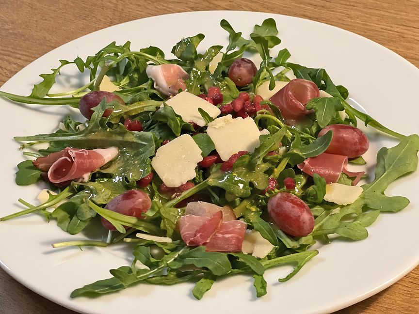 Rucola mit Schwarzwälder Schinken, Parmesan, Trauben und Granatapfelkernen mit einer Traubenkernöl-Vinaigrette.