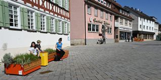 Sara Kurz und ihre Kinder beim Probesitzen auf den neuen Möbeln vor dem Alten Schulhaus. Im Hintergrund nach dem Gasthaus Hirsch und dem DRK-Kleiderladen steht die zweite Sitzgarnitur. Bild: Reichert