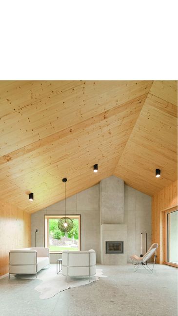Ein  großer Raum mit viel  Holz: Wohnbereich des von Rolf Klärle entworfenen Hauses mit großem quadratischen Fenster, bodentiefer Terrassentür und Kamin.