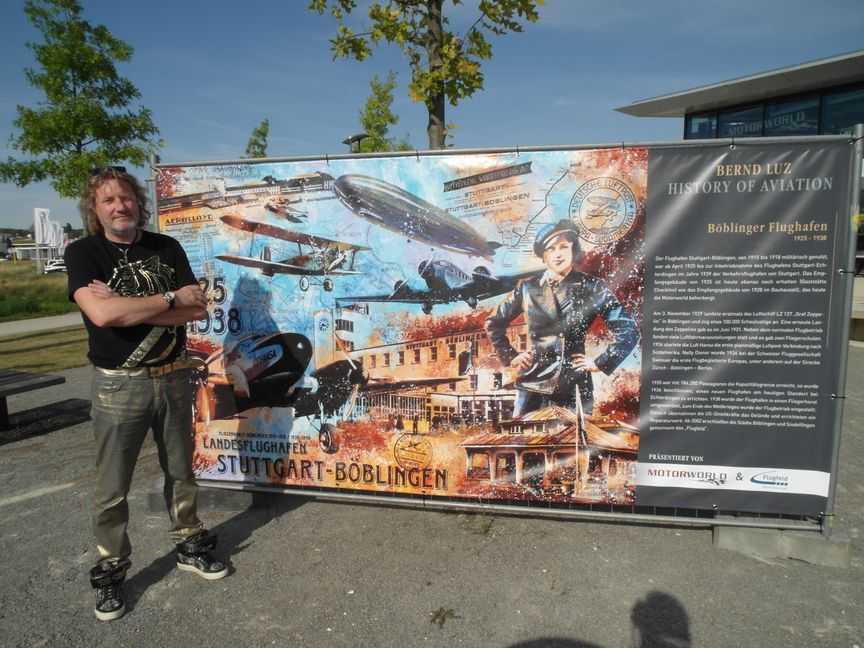 Der Künstler Bernd Luz aus Neuhausen ob Eck vor einem seiner Bilder, die er auf LKW-Plane gezogen und an einem Bauzaun installiert hat - dieses Bild beschäftigt sich mit der Geschichte des Flugfelds. Bild: Staber