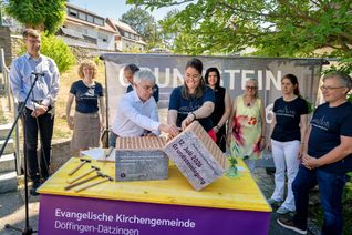 Die Zeitkapsel wird gemeinsam von Pfarrerin Brigitte Frauendorfer und dem Vorsitzenden der Kirchengemeinde Martin Tomtschko in den Mauerstein eingelegt. Rechts Björn Haßelkus, Bauauschuss-Vorsitzender.