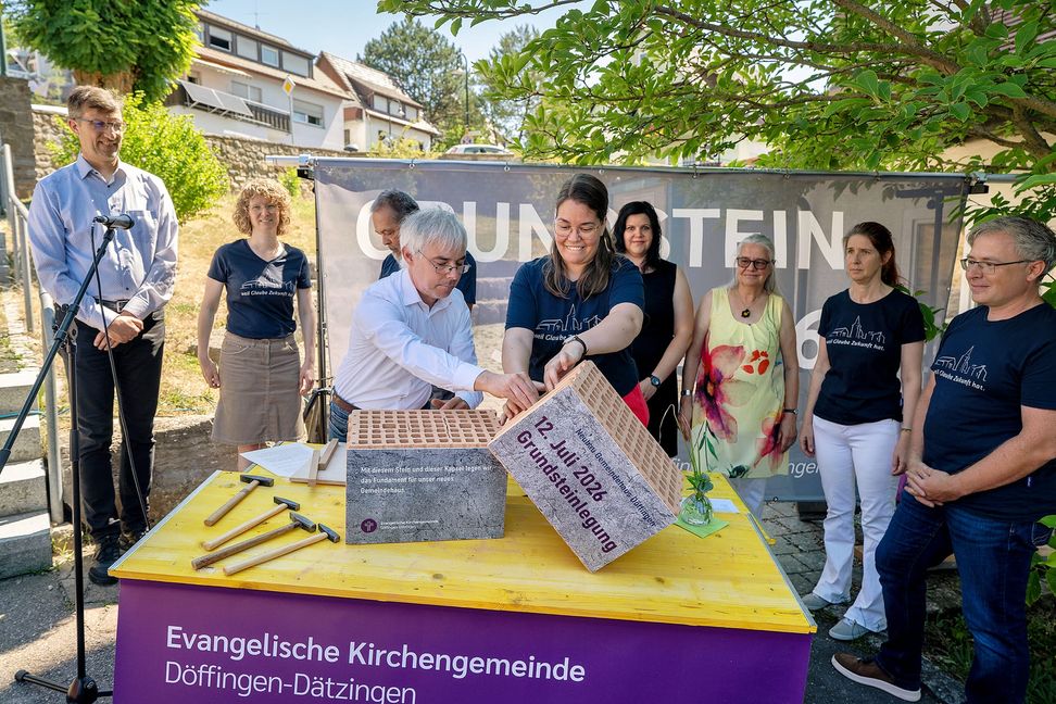 Die Zeitkapsel wird gemeinsam von Pfarrerin Brigitte Frauendorfer und dem Vorsitzenden der Kirchengemeinde Martin Tomtschko in den Mauerstein eingelegt. Rechts Björn Haßelkus, Bauauschuss-Vorsitzender.