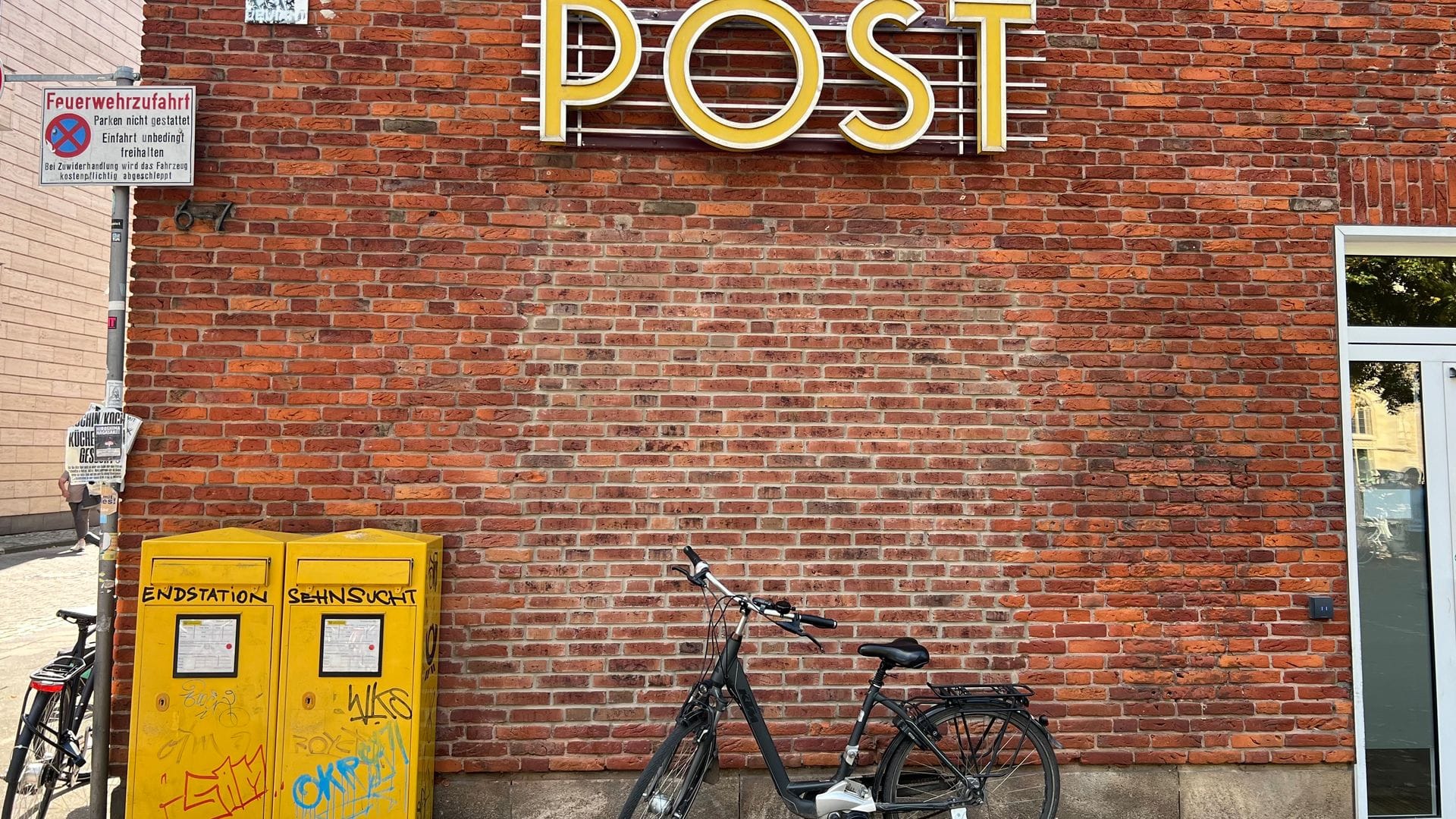 Ein Fahrrad steht vor einer Filiale der Postbank, die als Postfiliale fungiert. Anderswo in Deutschland gibt es keine Postfilialen, obwohl es sie einer staatlichen Vorschrift zufolge geben müsste.