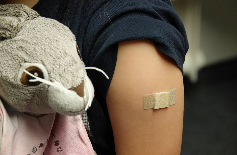Ein Pflaster klebt nach der Corona-Impfung in Essen auf dem Arm eines Mädchens, das ein Kuscheltier in den Händen hält.
 Foto: dpa/Mona Wenisch
