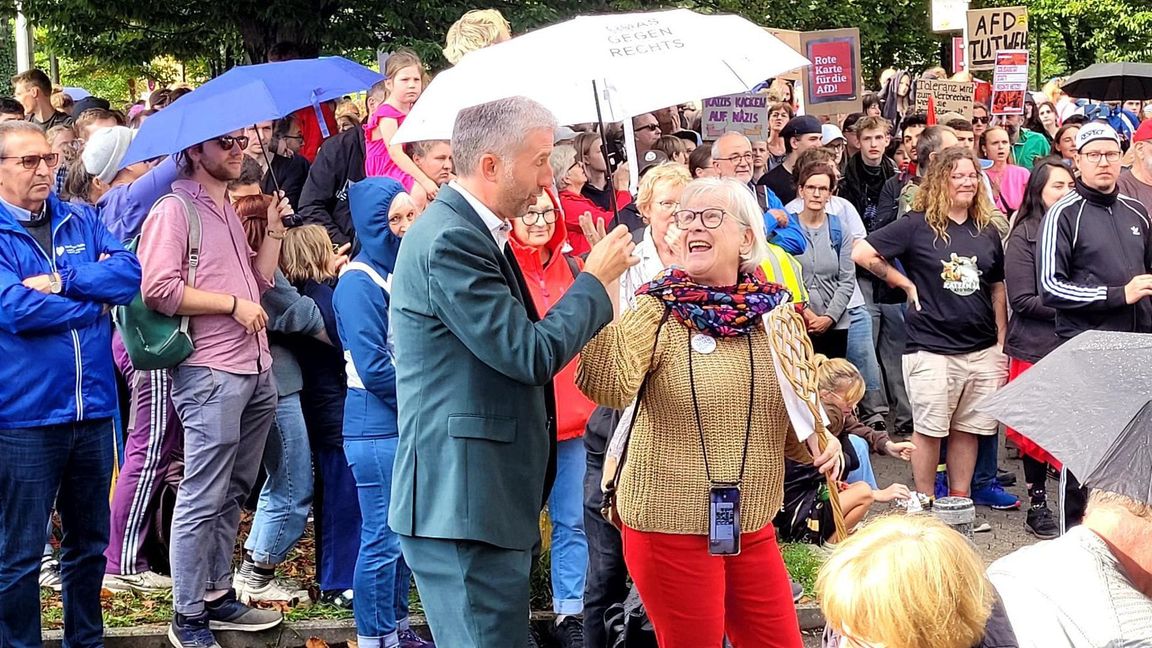 Es regnet kurzzeitig. Eine Frau reicht Palmer einen Schirm.