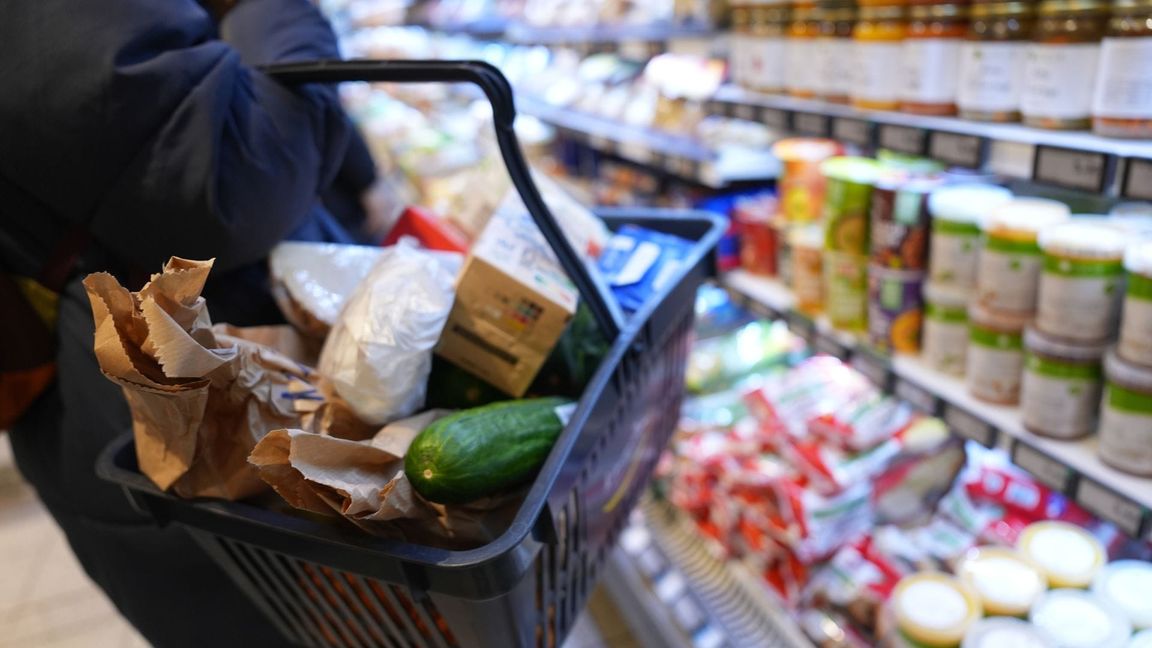 Eine Kundin geht mit einem Einkaufskorb und ihrem Einkauf an den Regalen in einem Supermarkt vorbei.