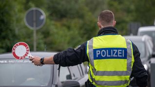 Ein Polizist hält Fahrzeuge an der Grenze zu Deutschland an.