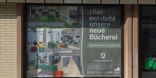Das Plakat hängt schon im Schaufenster des Gebäudes gegenüber von der Bücherei und zeigt, wie es nach dem Umbau und dem Umzug innen aussehen könnte. Bild: Reichert