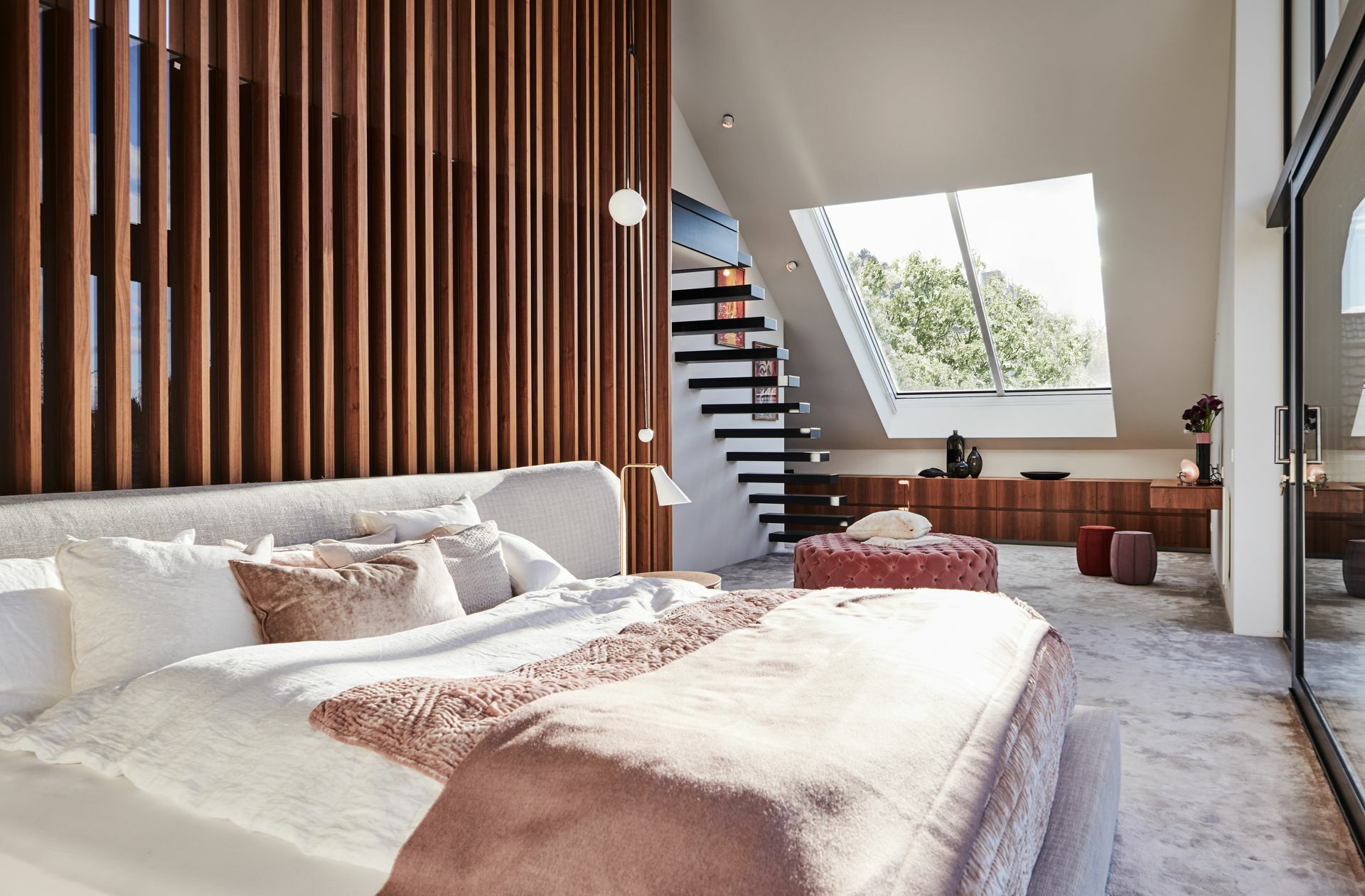 Schlafzimmer mit Aussicht. Hinter den Holzstäben verbirgt sich ein großzügiges Badezimmer. Die Treppe führt hinauf in einen Raum unterm Dach.