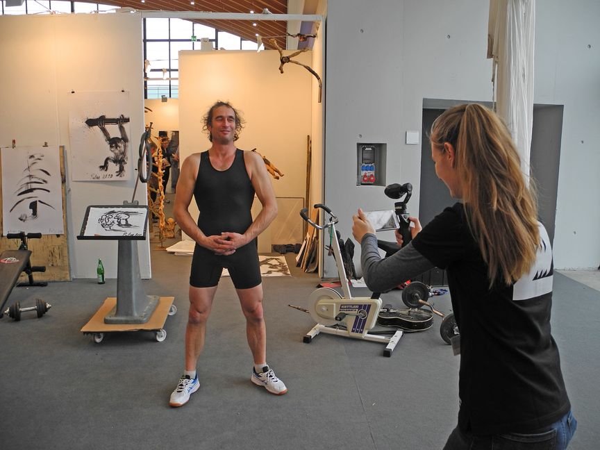 Bildhauer Thomas Putze wird bei seinem „Kraftakt“ auf der Art Karlsruhe von einem Fernsehteam gefilmt.  Bild: Volkmann