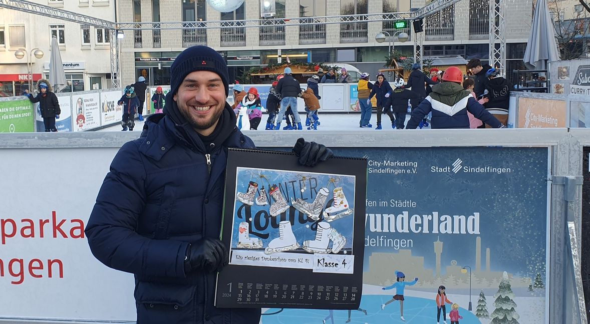 Salvatore Romeo strahlt übers ganze Gesicht. Zum einen freut er sich über das Kinderlachen hinter ihm, dazu auch über den von den Schülern gebastelten Kalender.     Bild: Wegner
