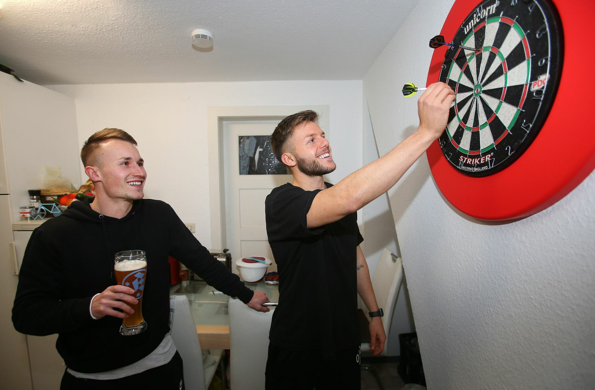 Moos (mit einem alkoholfreien Weizenbier) und Kammerbauer  haben Spaß beim Darts spielen.
 Foto: Baumann