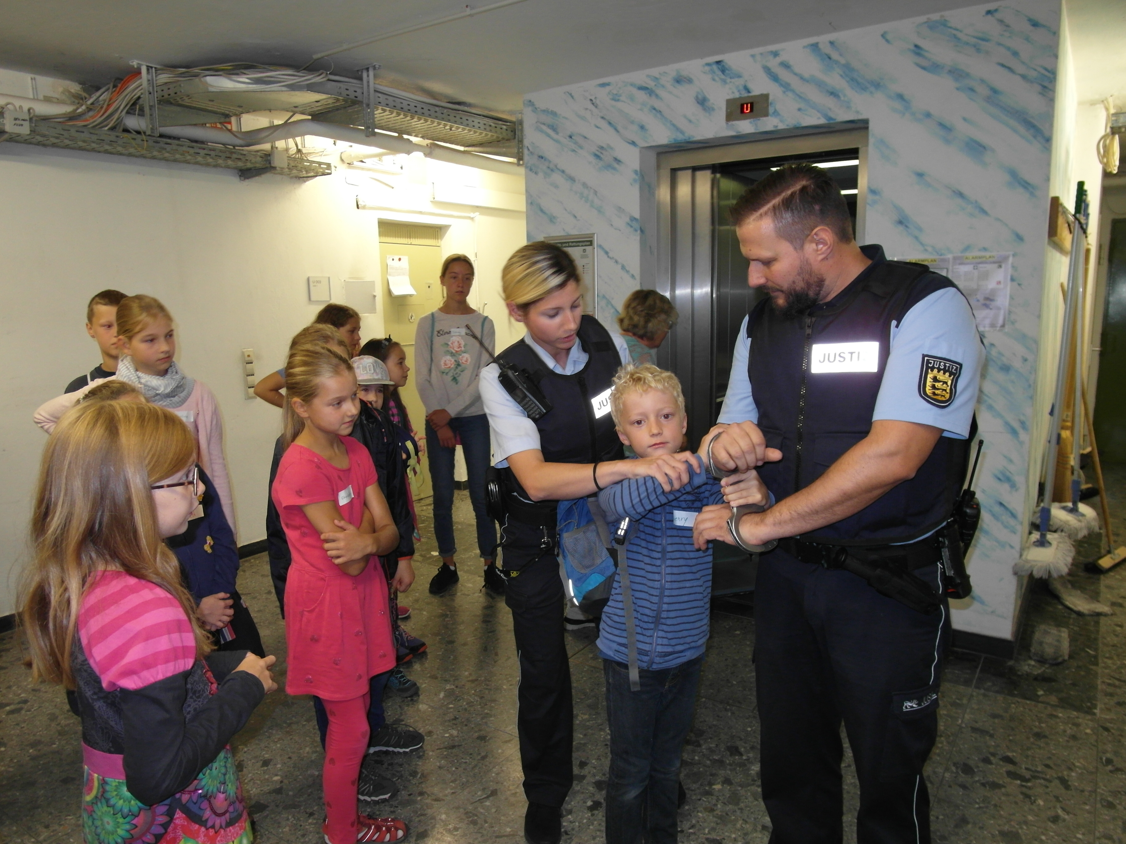 Wachtmeister Senad Ajkuvic lässt sich von einem teilnehmenden Kind des Ferienprogramms des Vereins "Prävent Sozial" Handschellen anlegen, um deren Funktionsweise zu erklären - unterstützt wird er dabei von Kollegin Kerstin Horvath. Bild: Staber