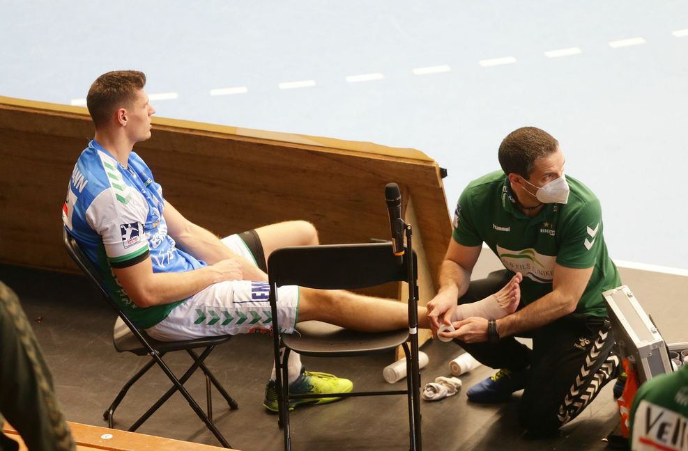 Sebastian Heymann von Handball-Bundesligist Frisch Auf Göppingen sitzt nach seiner Sprunggelenksverletzung am Spielfeldrand – Physiotherapeut Sebastian Daebel kümmert sich um die medizinische Erstversorgung. Foto: Baumann