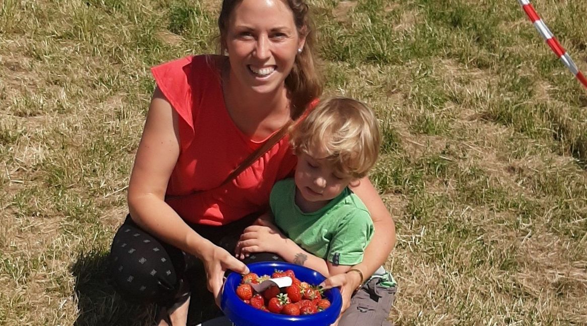 Anne Jüttner zeigt ihren Kindern, wie man Erdbeeren pflückt. Bild: Elbers