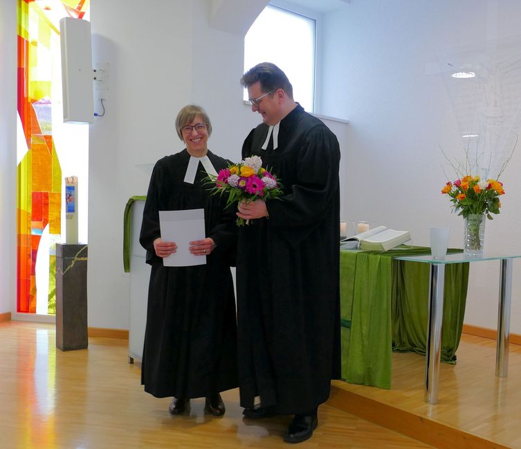 Dekan Markus Frasch überreicht seiner neuen Kollegin Pfarrerin Dr. Beate Kobler Urkunde und Blumen. Sie hilft ihm nun, den Kirchenbezirk zu verwalten. Bild: Lück