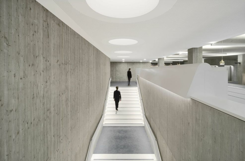 Im Neubau führt die Treppe von der Straßenebene und der Cafeteria  hinauf ins Foyer mit der zentralen Theke.
