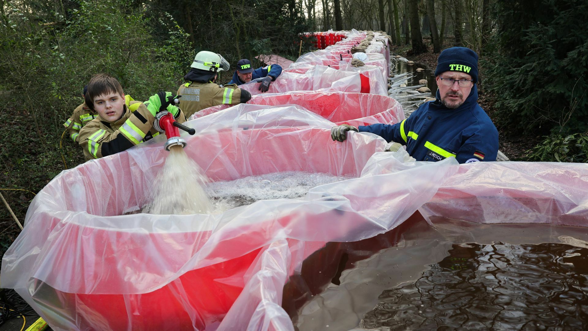 Niedersachsen, Oldenburg: Mitarbeiter von THW und der Feuerwehr Oldenburg befüllen Elemente eines mobilen Notdeichs mit Wasser. Der mobile Deich wird neben dem Parkfriedhof Bümmerstede errichtet.   Foto: dpa/Christian Charisius