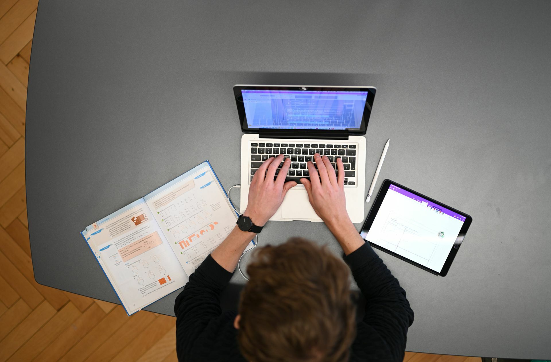 Multimedia in der Schule: Ein Mathelehrer setzt  Schulbuch, Laptop und Tablet im Fernunterricht mit seinen Schülern ein.