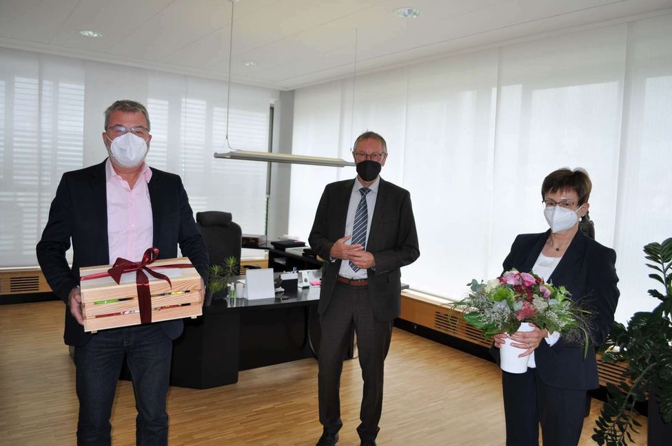 Auf dem Foto zu sehen: Landrat Roland Bernhard (Mitte) mit  Karin Bieber-Machner (rechts) und Holger Esch (links) bei der Verabschiedung durch Landrat Bernhard. Als Geschenke erhielten Karin Bieber-Machner und Holger Esch große Heckengäukisten mit Landkreis-Produkten, Blumensträuße sowie Herr Esch einen Restaurantgutschein und Frau Bieber-Machner einen Gutschein für das Staatstheater.    Bild: Landkreis Böblingen/z
